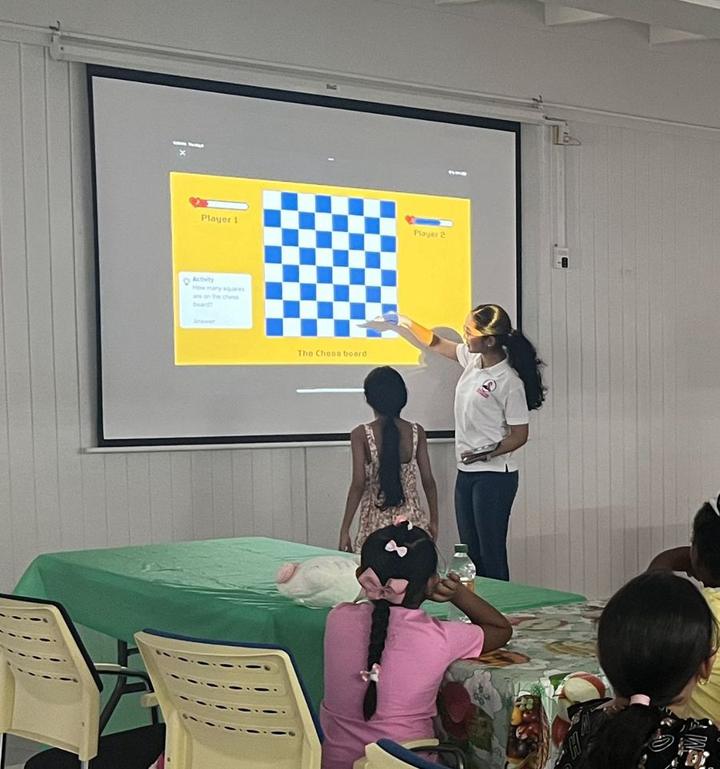 A mentor teaching children about the chessboard on a projector screen